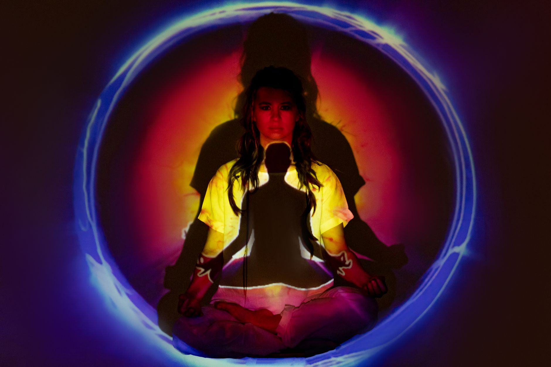 Person meditating cross-legged surrounded by a glowing ring of colorful light energy